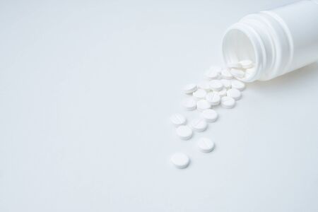 white pills are poured out of plastic packaging on a white background with copy spaceの写真素材