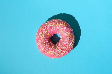 donut in pink glaze with colorful sprinkles on a blue backgroundの写真素材
