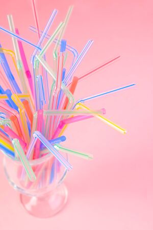 Multicolored plastic cocktail straws in an empty glass cup on a pink background. Concept: holiday, party, ecology, plasticの写真素材