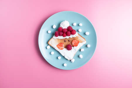 Childrens breakfast or lunch, toast stylized in the form of santa claus with raspberries, strawberries, cottage cheese and marshmello. New Years table decoration.の写真素材