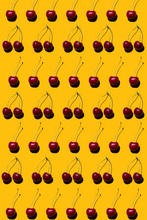 Ripe red cherry fruits on a yellow background. Bright pattern with hard shadows