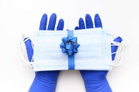 Hands in protective gloves hold protective masks tied with a shiny blue ribbon with a blue bow. Christmas present new year during the coronavirus pandemicの写真素材