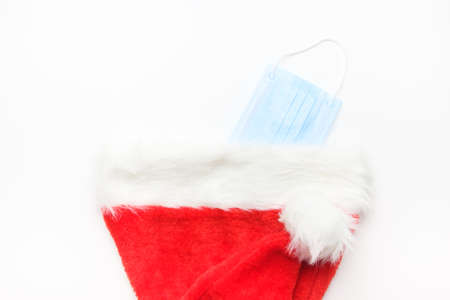 Disposable protective mask hidden in a Santa Claus hat. Stuff to celebrate New Years plans or Christmas wish list.の写真素材