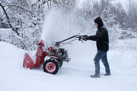 young man clearing snow in his backyard with wheeled snow blowerの写真素材