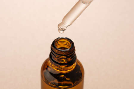 A bottle of essential oil with a glass pipette on a beige background. Natural skin care cosmetics.