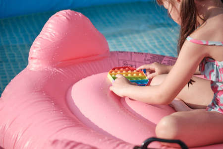 little cheerful girl plays in a multi-colored plastic toy pop it and swims in the pool. playing in the water during summer holidaysの写真素材