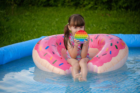 little cheerful girl plays in a multi-colored plastic toy pop it and swims in the pool. playing in the water during summer holidaysの写真素材