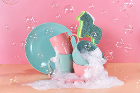 creative still life in bright colors with a sponge in the shape of a unicorn. The unicorn will say through the mountains of dirty dishes filled with foam for washing dishes surrounded by soap bubblesの写真素材