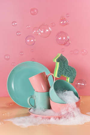 creative still life in bright colors with a sponge in the shape of a unicorn. The unicorn will say through the mountains of dirty dishes filled with foam for washing dishes surrounded by soap bubblesの写真素材