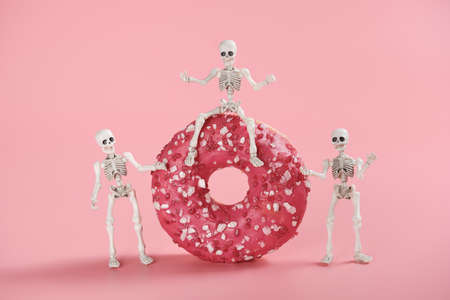 The skeleton sits astride a pink-glazed donut and two skeletons stand side by side. Bright image on...