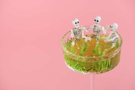 Three skeletons in a glass with a green drink on a pink background. Skeletons take a bath in a cocktail. Halloween party decorationsの写真素材