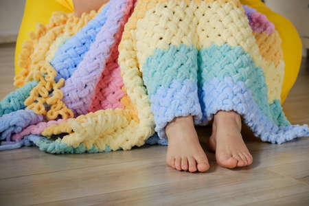 A young woman knits a warm bright plaid from multi-colored terry looped yarn with her hands. A cozy...