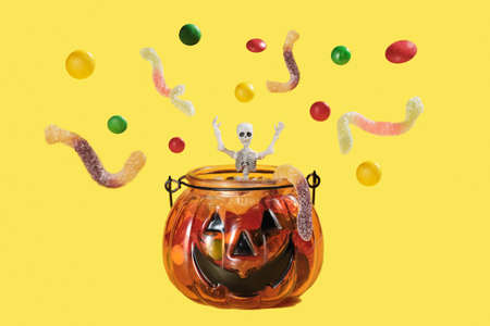 a skeleton figurine jumps out of a pumpkin-shaped vase of candy. around the skeleton, colorful...