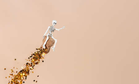 a human skeleton flies astride a champagne cork with a train of golden candy in the shape of...