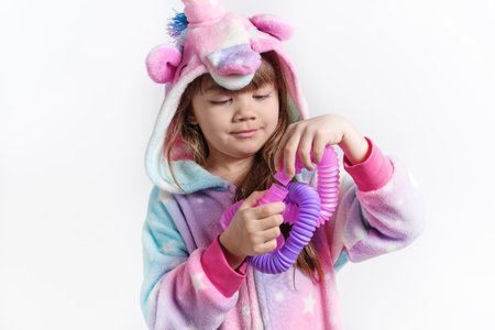 Cheerful little girl in unicorn pajamas plays in a popular toy poptube. An exciting childrens game with multi-colored plastic pipes.の写真素材