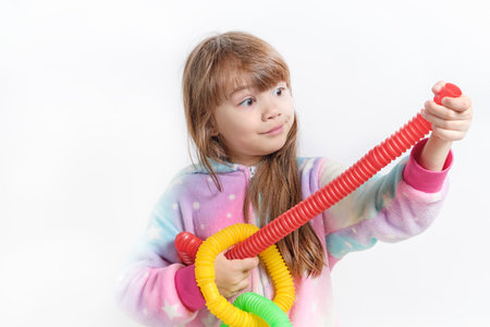 Cheerful little girl in unicorn pajamas plays in a popular toy poptube. An exciting childrens game with multi-colored plastic pipes.の写真素材