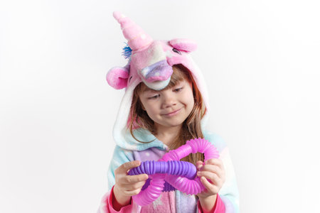 Cheerful little girl in unicorn pajamas plays in a popular toy poptube. An exciting childrens game with multi-colored plastic pipes.の写真素材