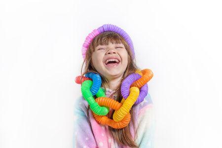 Cheerful little girl in unicorn pajamas plays in a popular toy poptube. An exciting childrens game with multi-colored plastic pipes.の写真素材