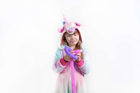 Cheerful little girl in unicorn pajamas plays in a popular toy poptube. An exciting childrens game with multi-colored plastic pipes.の写真素材