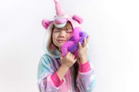 Cheerful little girl in unicorn pajamas plays in a popular toy poptube. An exciting childrens game with multi-colored plastic pipes.の写真素材