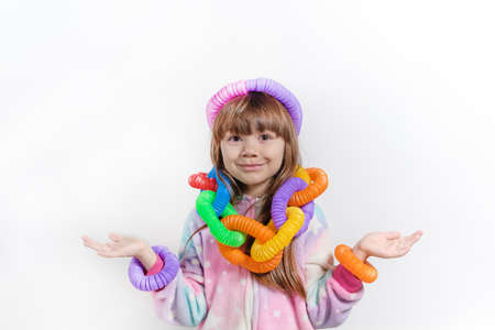 Cheerful little girl in unicorn pajamas plays in a popular toy poptube. An exciting childrens game with multi-colored plastic pipes.の写真素材
