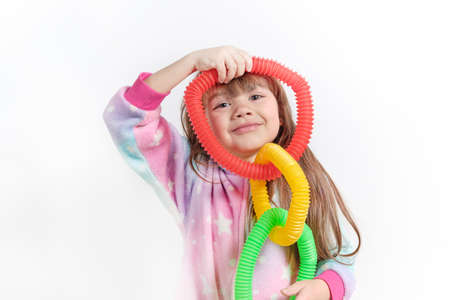 Cheerful little girl in unicorn pajamas plays in a popular toy poptube. An exciting childrens game with multi-colored plastic pipes.の写真素材
