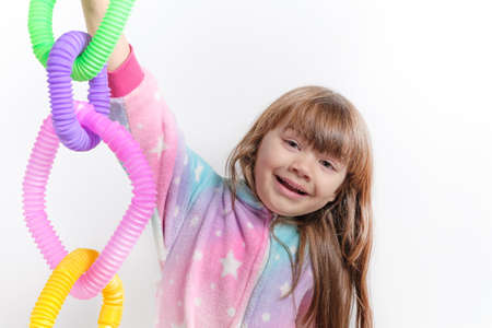 Cheerful little girl in unicorn pajamas plays in a popular toy poptube. An exciting childrens game with multi-colored plastic pipes.の写真素材