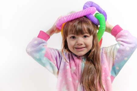 Cheerful little girl in unicorn pajamas plays in a popular toy poptube. An exciting childrens game with multi-colored plastic pipes.の写真素材