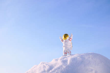 a small toy figurine of an astronaut with arms raised up against the blue sky stands on top of a snowy mountainの写真素材