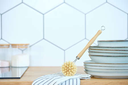 eco-friendly dishwashing brushes with organic bristles and a wooden handle next to a stack of clean dishes on the kitchen table. The concept of minimum consumption, zero-waistの写真素材