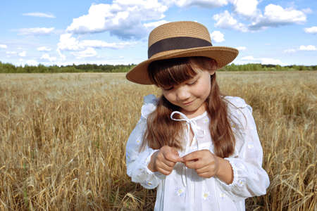 A little girl in a white dress and a straw hat plays with a toy plane in a rye field inの写真素材