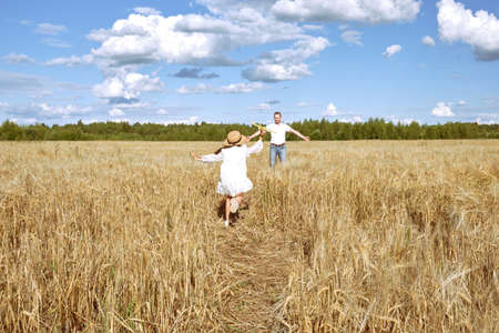 A little girl in a white dress and a straw hat plays with a toy plane in a rye field in