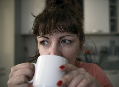 Young woman drinking coffee in the morning in the kitchen, tired eyes with red veinsの写真素材