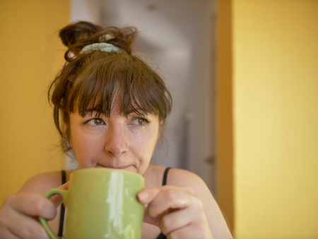 Sad and sleepy young woman with a cup of coffee in the morning at homeの写真素材