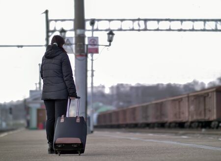 A lonely girl with a black suitcase is standing on the platform.