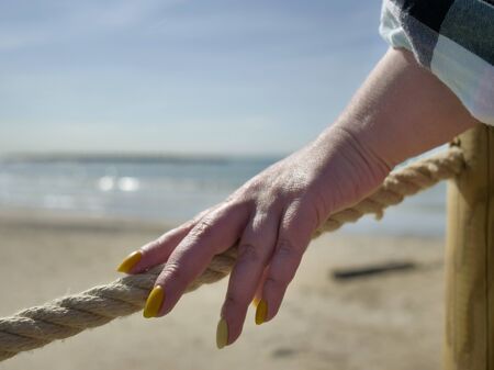 A female hand touches a rope stretched on a beach pier near the sea, the passage is closed, the end of the beach seasonの写真素材