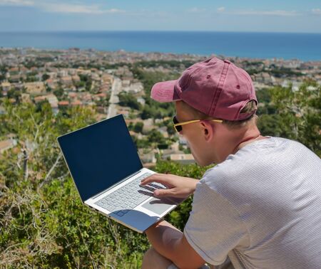 Portrait of a freelancer working on a laptop on a mountain near a seaside townの写真素材