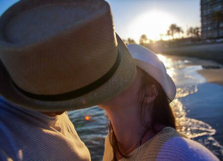 Loving couple in hats kisses on the seashore during sunset, close-upの写真素材