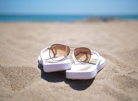White female slippers and sunglasses on a sandy beach, vacation concept, close-upの写真素材