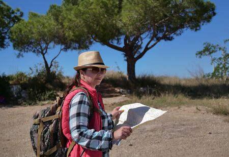 Traveler girl with a backpack and a map on nature inspects the terrain.