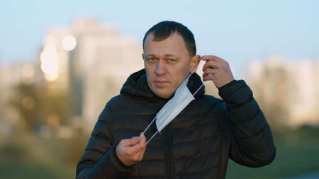 Young man standing on the street putting on a disposable medical mask
