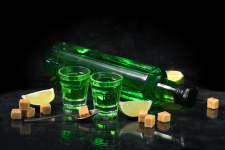 green absinthe drink on the black background with sugar and lime