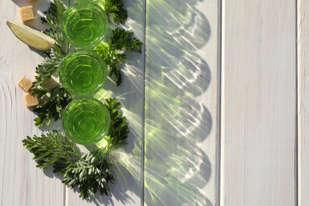 Glasses of green absinthe on white wooden table, top view