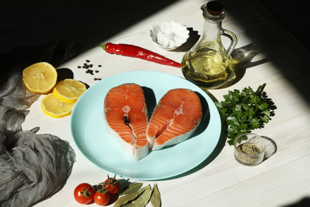 Fresh salmon steak with ingredients on blue plate and white wooden backgroundの写真素材