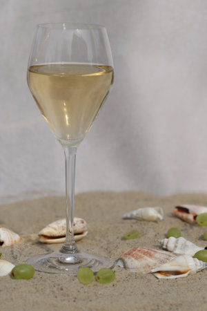 glass of white wine on sand as background with shellsの写真素材