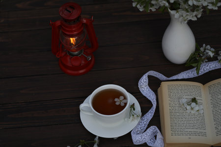 cup of tea with cherry blossom decoration on dark brown wooden background. Bouquet, book and kerosene lampの写真素材
