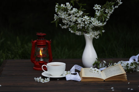 cup of tea with cherry blossom decoration on dark brown wooden background. Bouquet, book and kerosene lampの写真素材