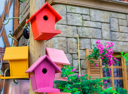 Multicolored nesting boxes birdhouses outdoor with a part of house stone wall with window on the backgroundの写真素材