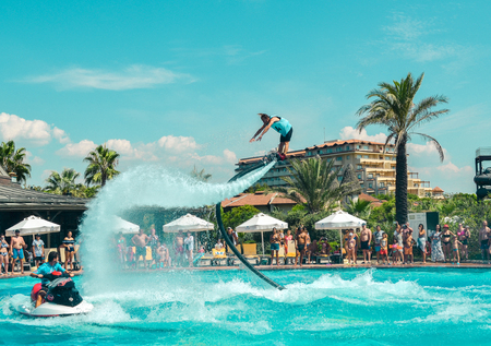 Belek, Turkey - September 12, 2018. Exciting fly board watershow at the pool party on a sunny summer day. A man is doing acrobatics with flyboard attached to jet ski with spectators on the back.のeditorial素材