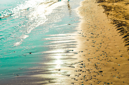 Turquoise sea and golden sand beach with small pebbles covered by sunlight backlight. Way to the dream, light, energy and balance concept.の写真素材